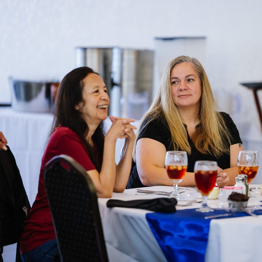 Two women laughing together at a table at the HCISD retiree dinner