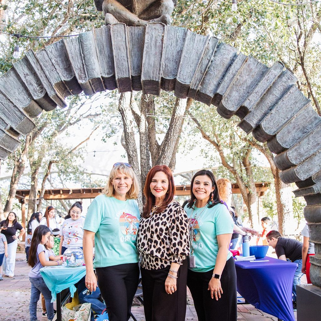 Three smiling HCISD staff members under the stone arch at the Harlingen Public Library literacy night